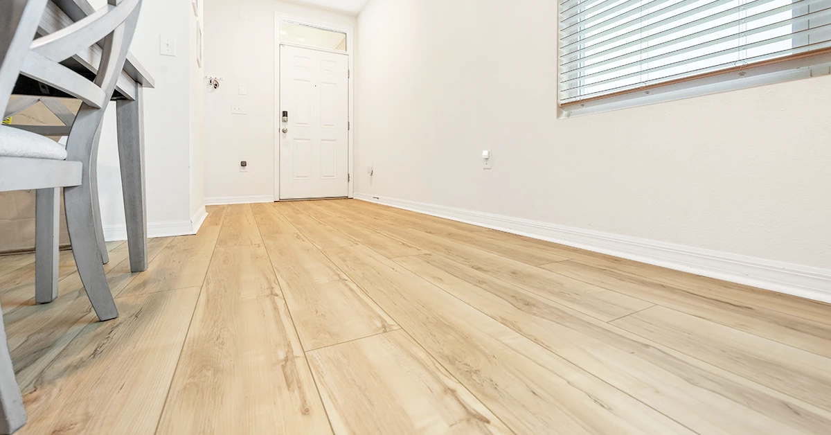 A serene, sunlit entryway featuring light oak-look flooring, crisp white baseboards, and a modern gray chair — perfect for showcasing timeless, elegant flooring design.