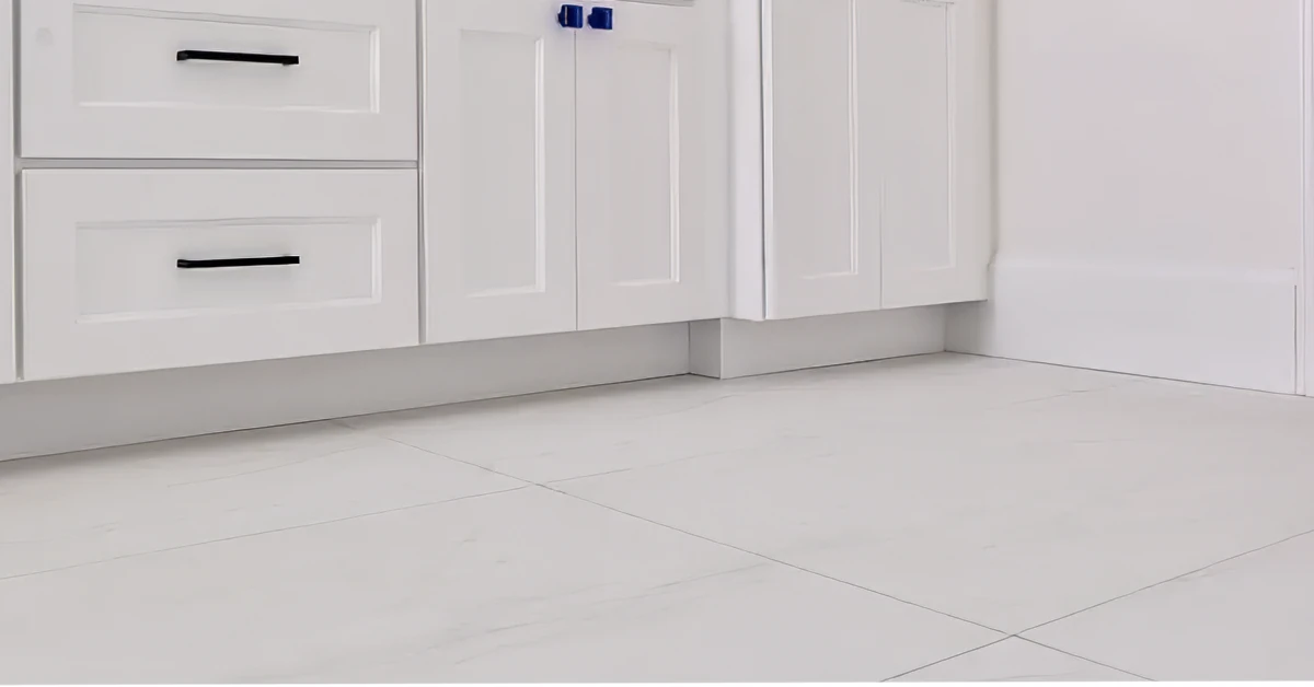 Detailed view of elegant white tile flooring beneath sleek white kitchen cabinets, emphasizing clean lines and a polished finish.