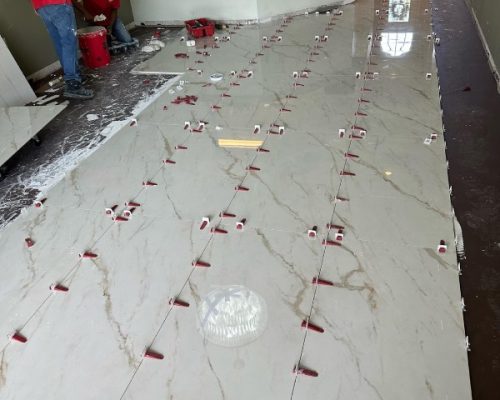 Large-format white porcelain tiles being professionally leveled during flooring installation service