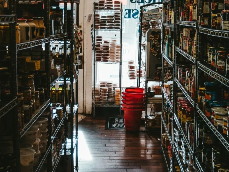 Durable dark wood-style flooring runs through a compact retail aisle flanked by metal shelving units filled with products, enhancing the store’s professional and inviting atmosphere.