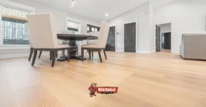 A bright, modern dining area featuring beautiful light-toned vinyl plank flooring extending into the hallway, with contrasting dark doors.
