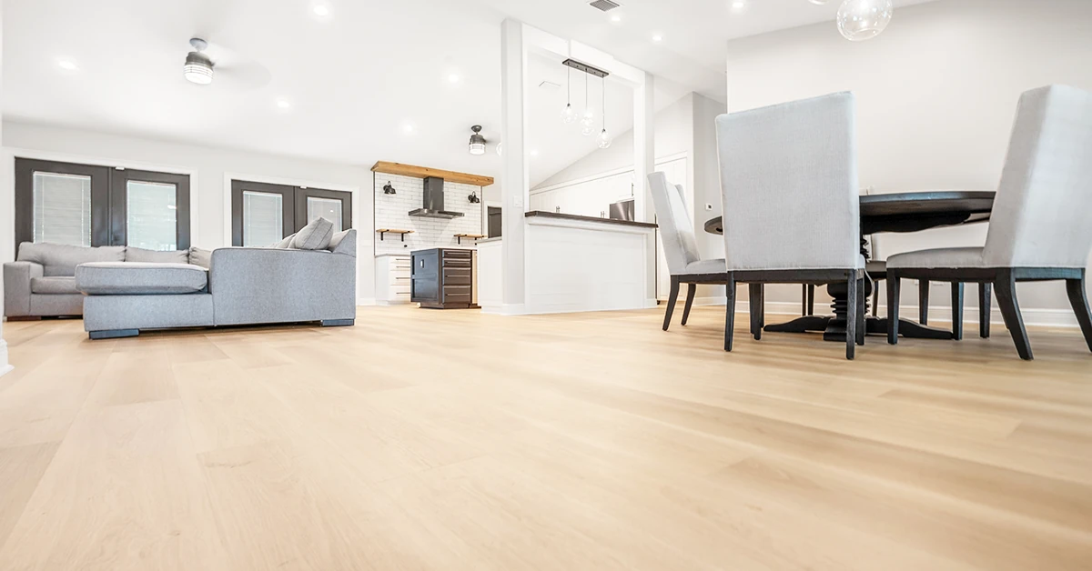 Expansive view of smooth, light-colored vinyl plank flooring flowing through a bright, open-plan living and dining area with modern furnishings and natural lighting.