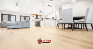Open concept living space with a dining area, living room, and kitchen, unified by seamless light-colored vinyl plank flooring.