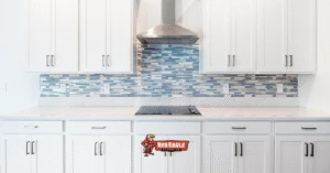 Clean, modern kitchen with white cabinets, a light countertop, and a striking blue glass mosaic backsplash above the cooktop. This is an example of design elements surrounding Kitchen and Bathroom Flooring.