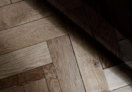 Detailed view of premium wood-grain vinyl planks installed in a herringbone pattern, highlighting craftsmanship and the interplay of light and shadow on the surface.