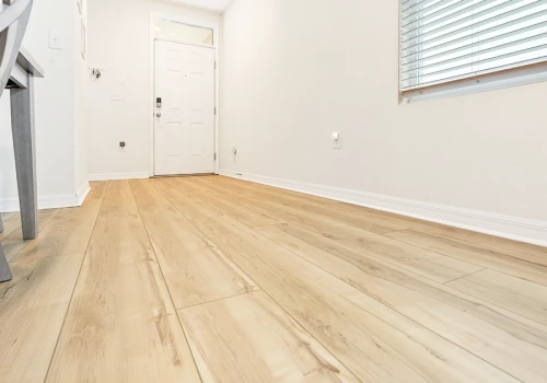 A serene, sunlit entryway featuring light oak-look flooring, crisp white baseboards, and a modern gray chair — perfect for showcasing timeless, elegant flooring design.