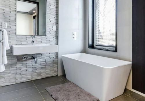 Elegant bathroom showcasing a textured gray mosaic tile accent wall behind a floating sink, paired with large-format floor tiles and a minimalist freestanding tub.