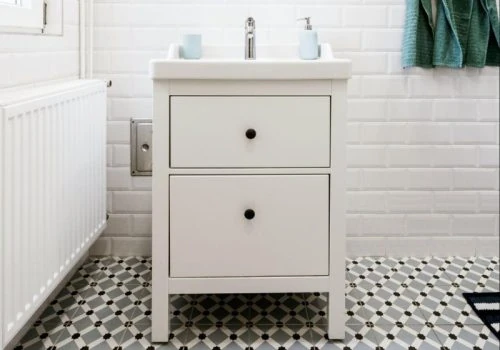 A modern bathroom featuring white subway tile walls, a compact white vanity, and a striking black-and-white geometric tile floor — ideal for cost estimation discussions.