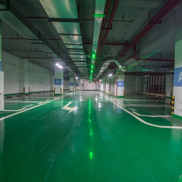 High-gloss green epoxy flooring with white lane markings and “A1” zone signs in a spacious, modern underground parking garage with visible structural columns and lighting.