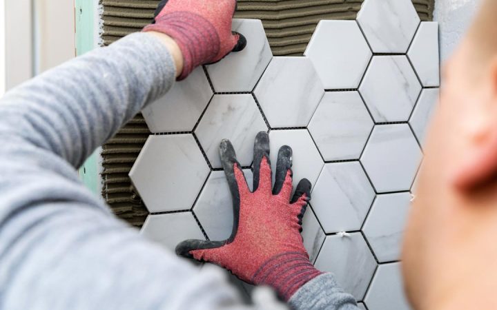 An expert tile installer placing hexagonal small tiles for a mosaic style for the wall